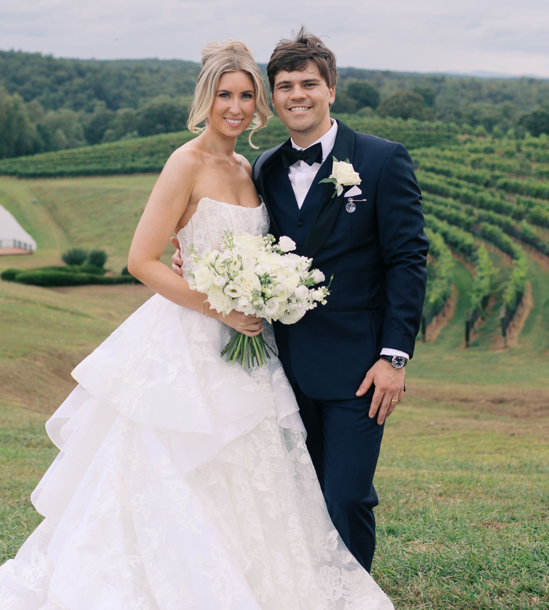 A bride and groom are posing for a picture in front of a vineyard.