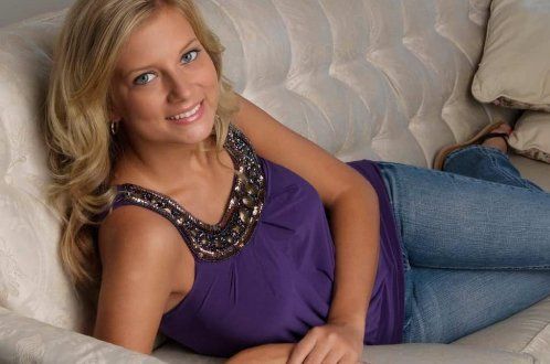 A woman in a purple tank top and jeans is laying on a couch.