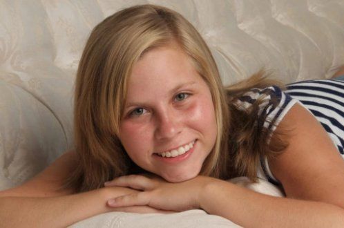 A blonde girl smiling, with a striped shirt on