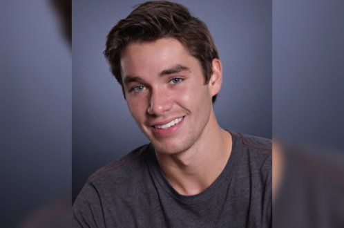 A young man in a grey shirt is smiling for the camera.