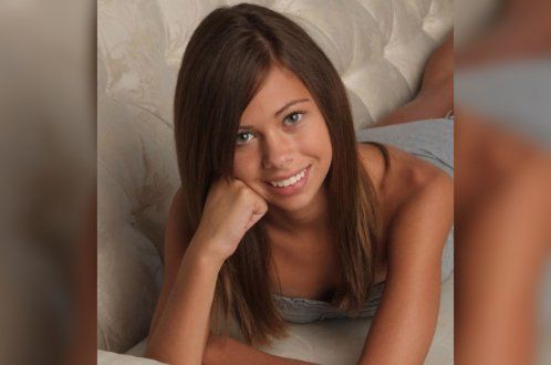 A woman is laying on a bed with her hand on her chin and smiling.