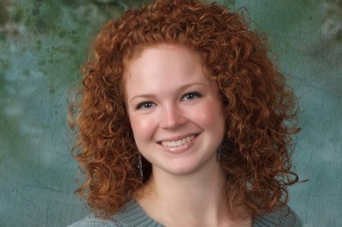 A woman with red curly hair is smiling for the camera.
