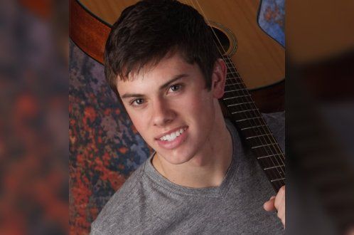 A young man is holding a guitar and smiling for the camera.