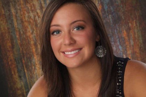 A woman in a black tank top and earrings is smiling for the camera.
