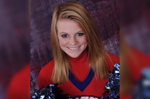 A cheerleader in a red and blue uniform is smiling for the camera.