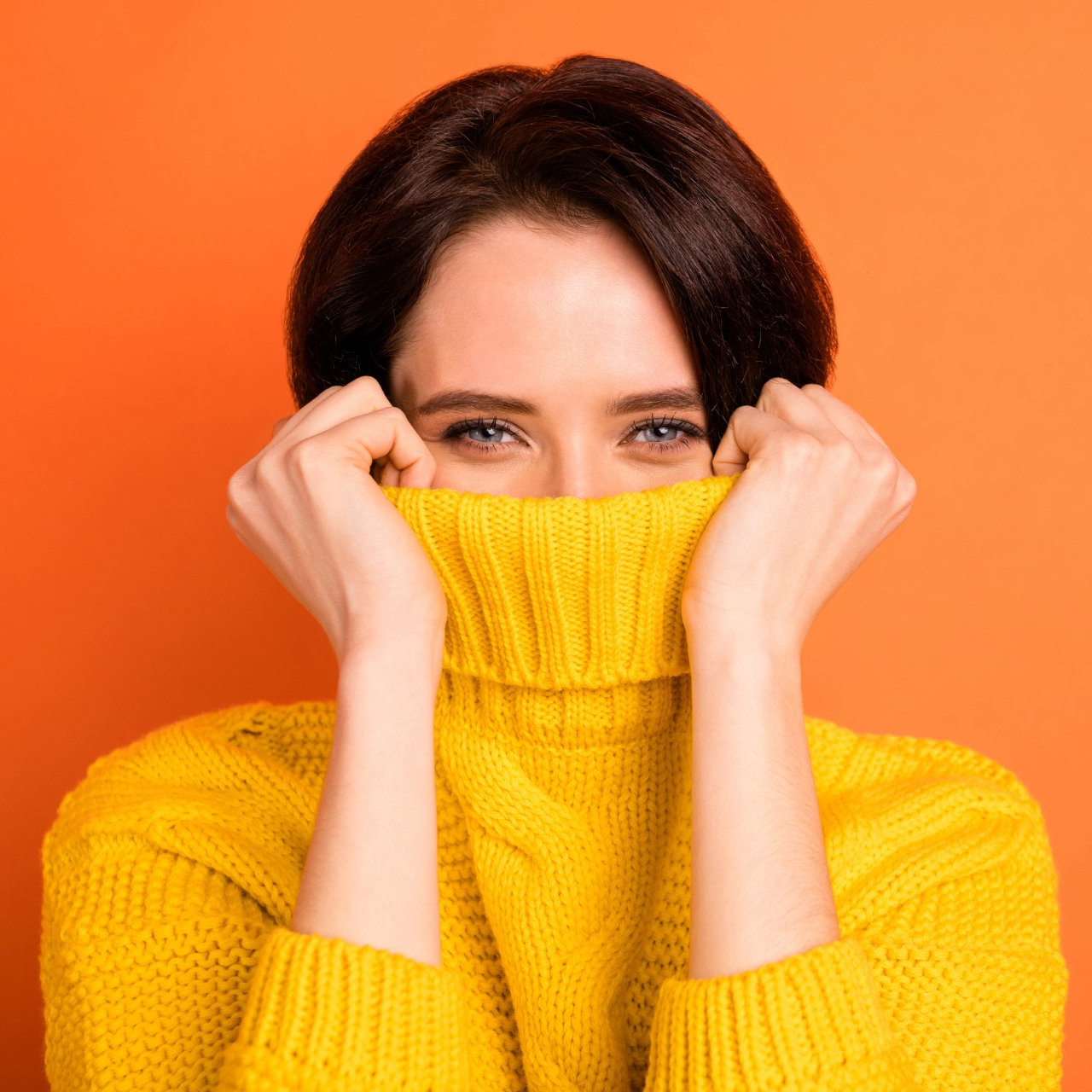 A woman in a yellow sweater is covering her face with her hands.