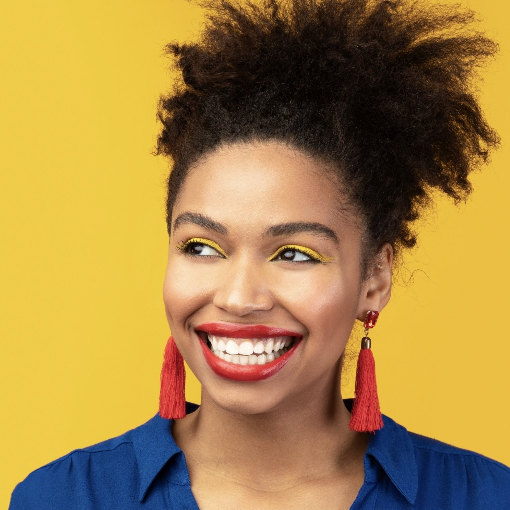 A woman wearing a blue shirt and red tassel earrings is smiling.