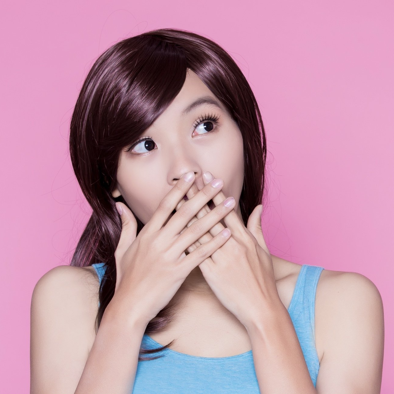 A woman covering her mouth with her hands on a pink background
