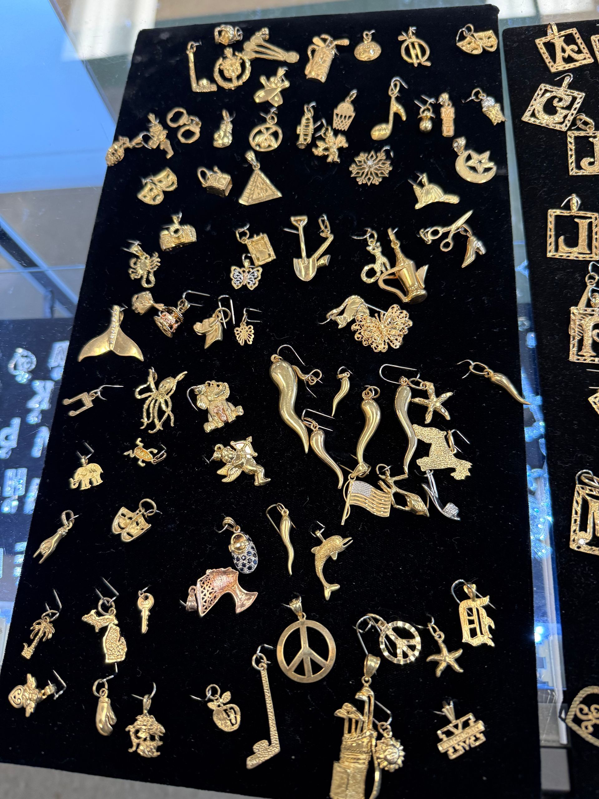Gold pendant charms displayed on black velvet, including crosses, hearts, figures, and symbols.
