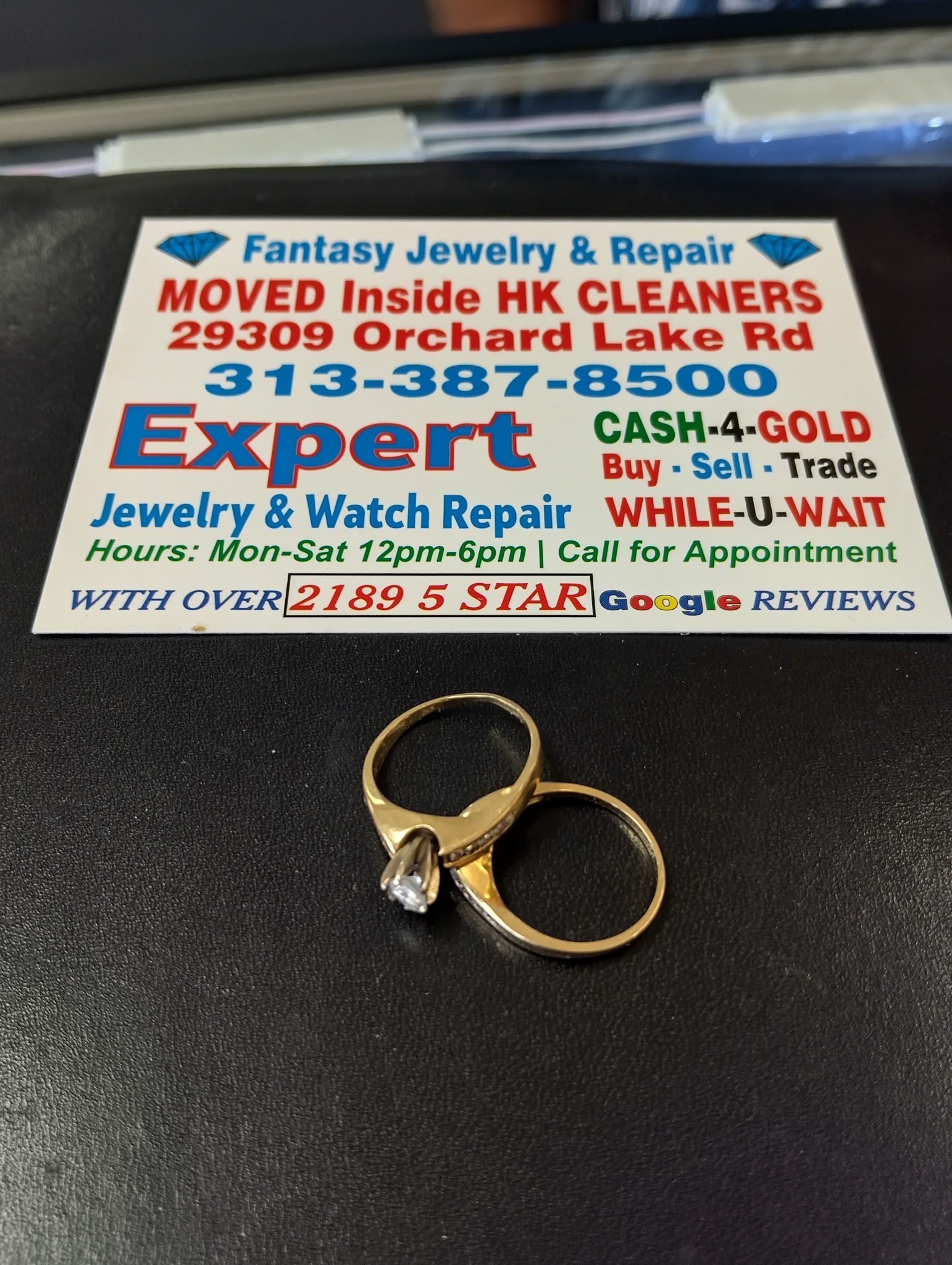 Two gold rings on a black surface beside a jewelry repair business card.