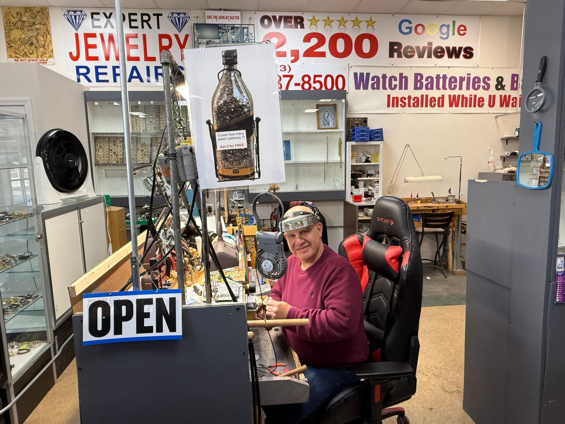 Jewelry repair shop counter with a seated worker and an OPEN sign in the foreground.