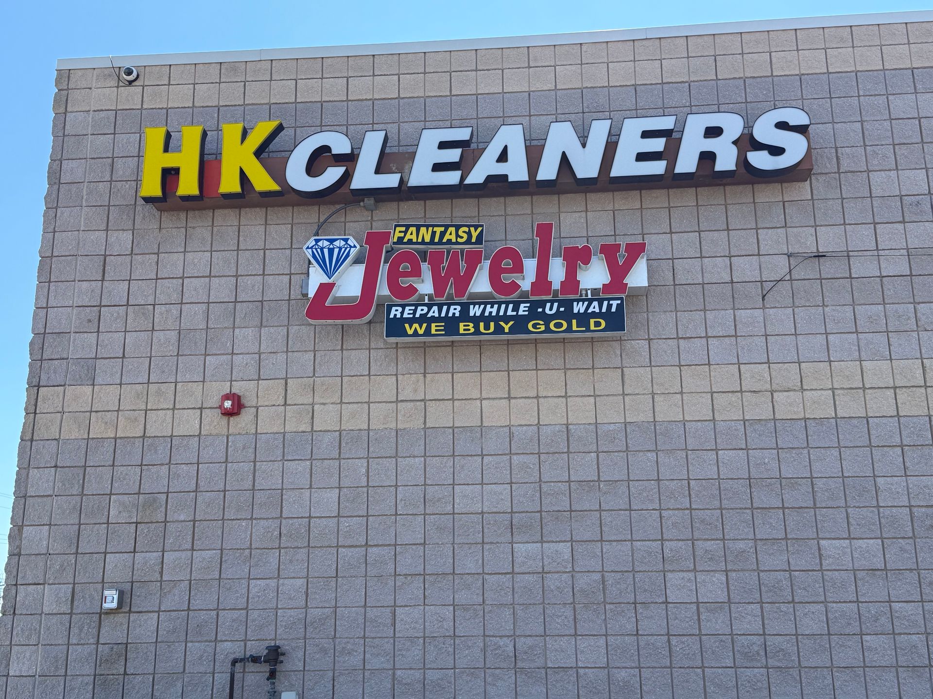 Storefront signs for HK Cleaners and a jewelry shop on a tan brick wall