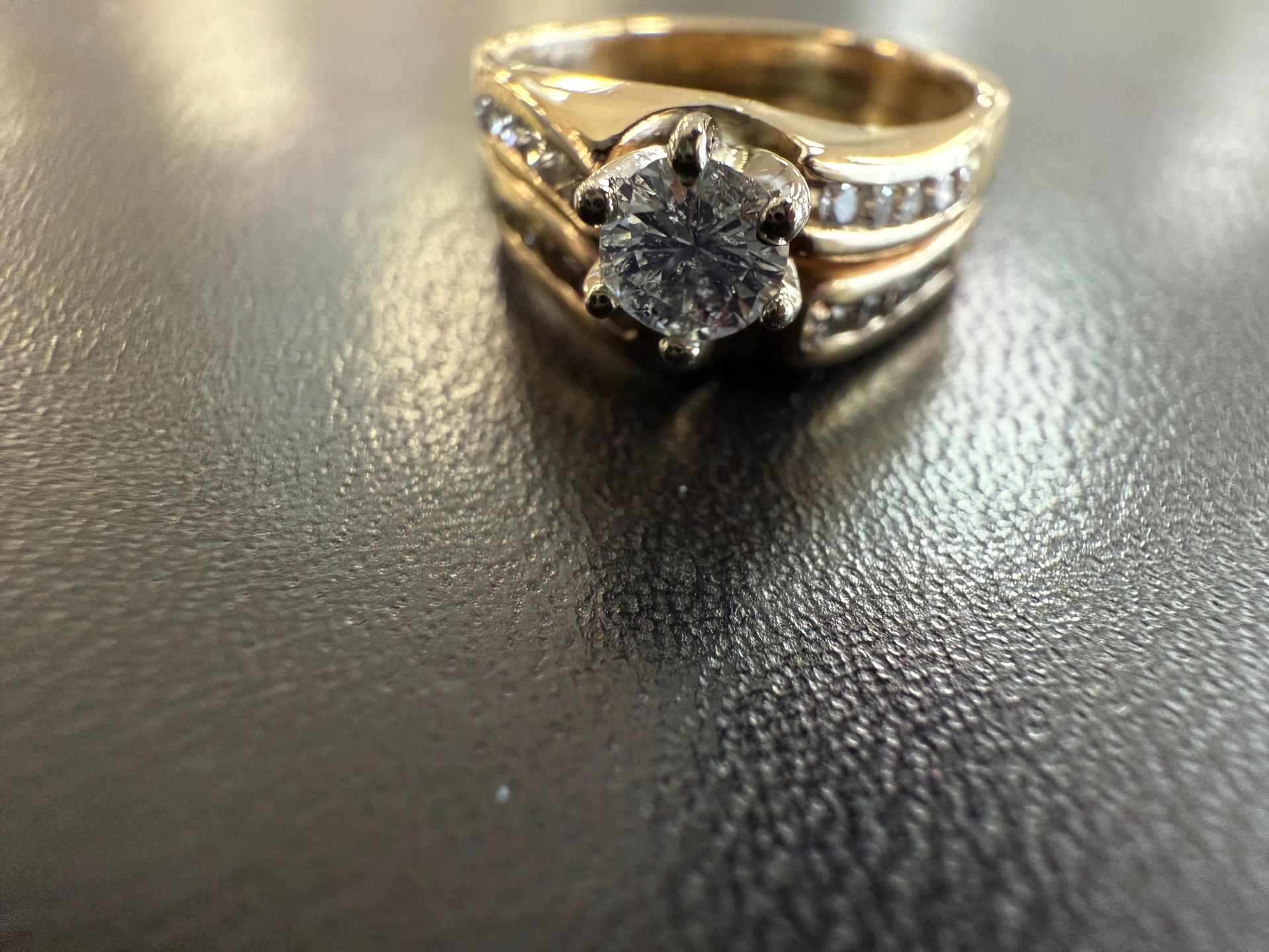 Diamond ring on a dark textured surface, with a gold band and silver accents