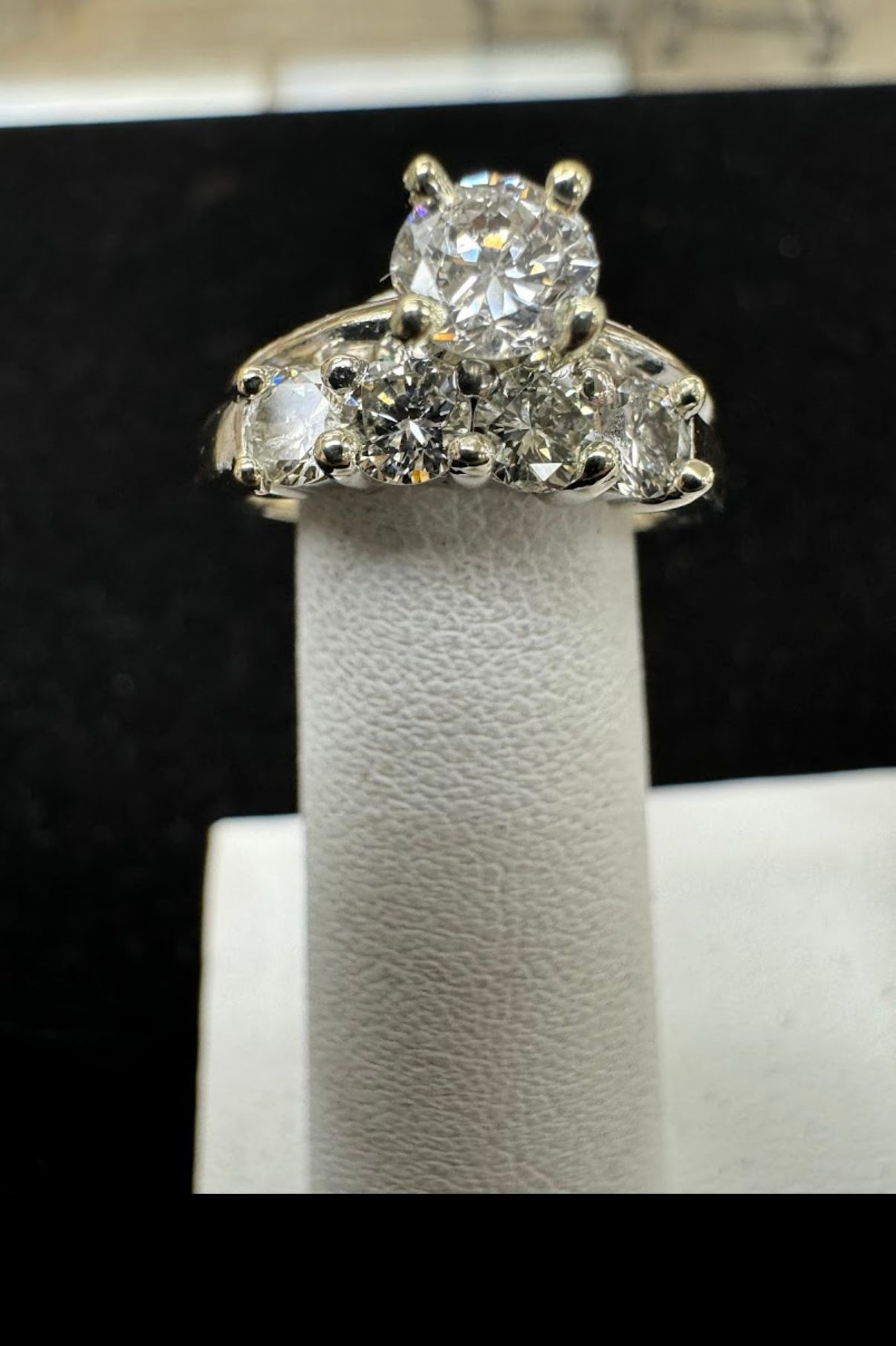 Diamond engagement ring on a white display stand against a black background