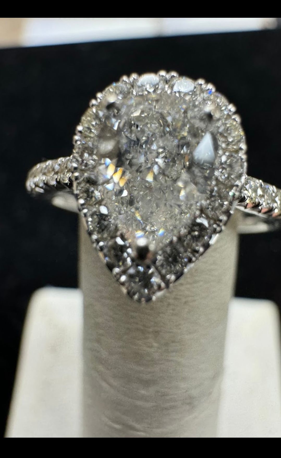 Pear-shaped diamond halo engagement ring on a display stand, with a split shank band
