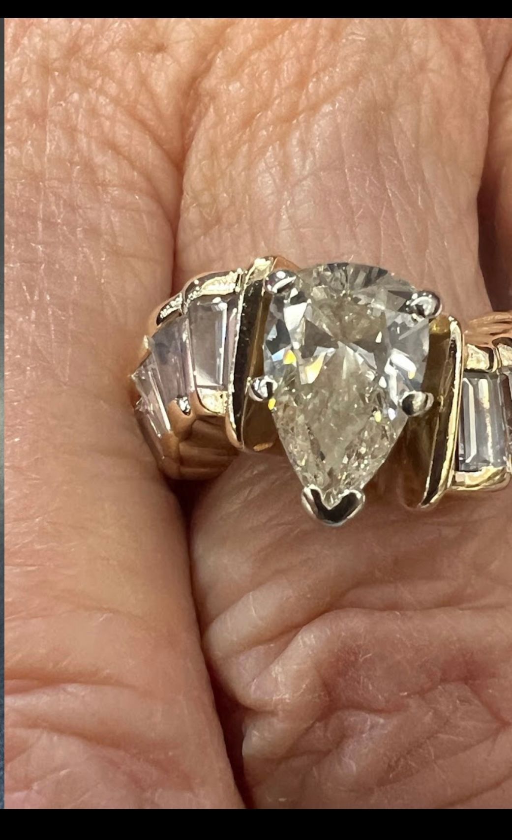 Close-up of a pear-shaped diamond ring on a wrinkled hand, set in gold and silver tones