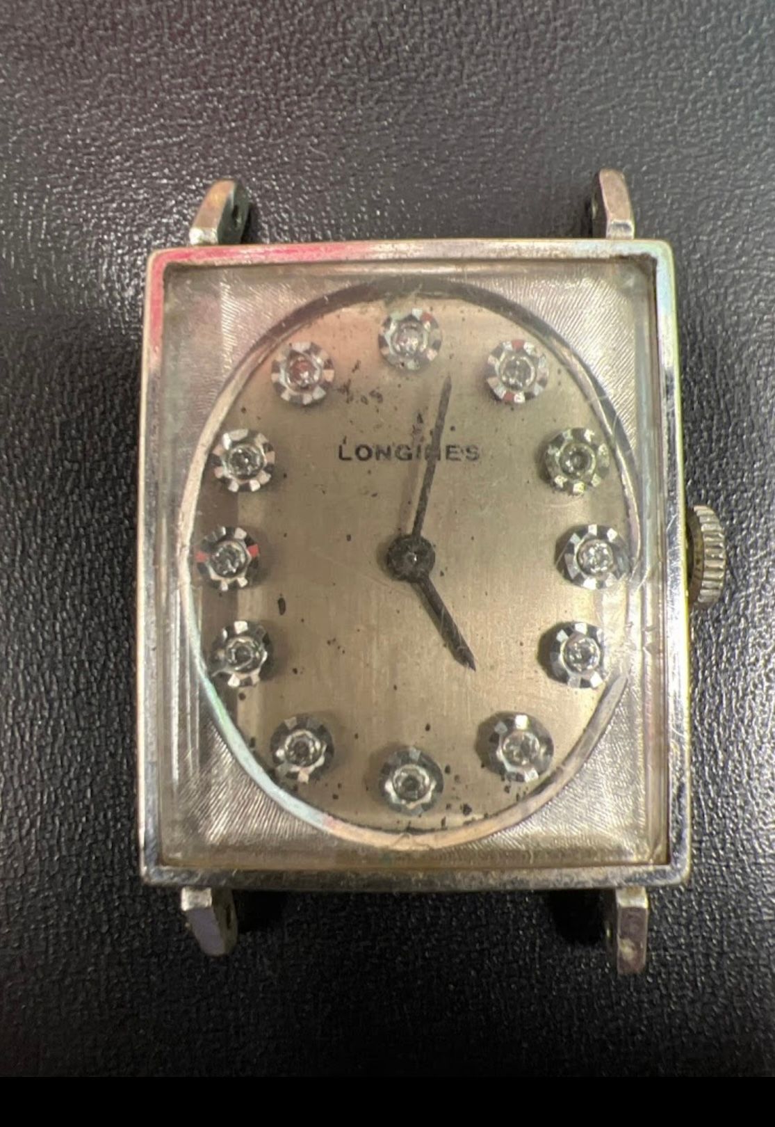 Vintage Longines wristwatch with a rectangular metal case and jeweled dial, showing a black hand on worn face