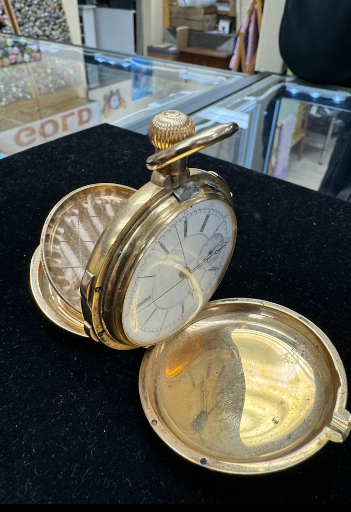 Gold antique pocket watch with open lid on a black display surface.