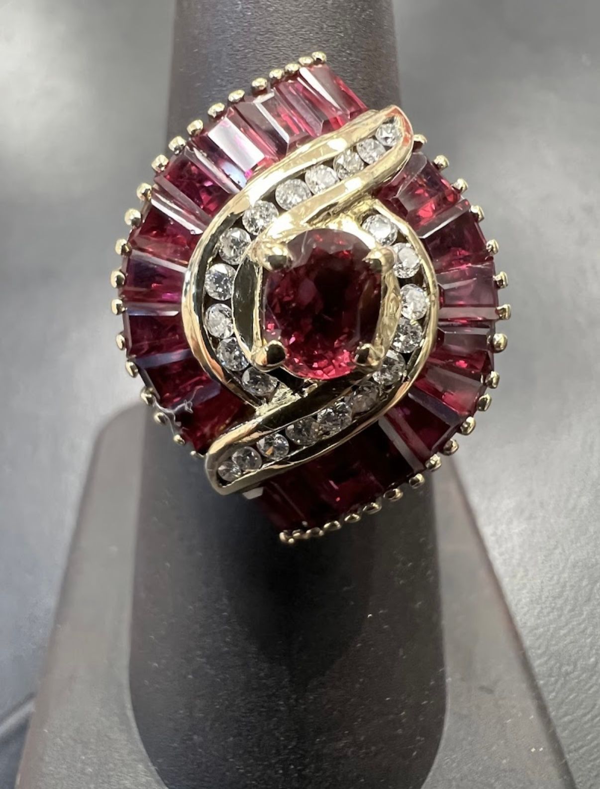 Close-up of a ruby and diamond ring with a deep red center stone on a dark display stand