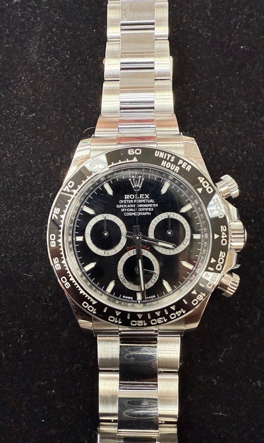 Black Rolex Daytona watch with silver bracelet and black dial on a dark background