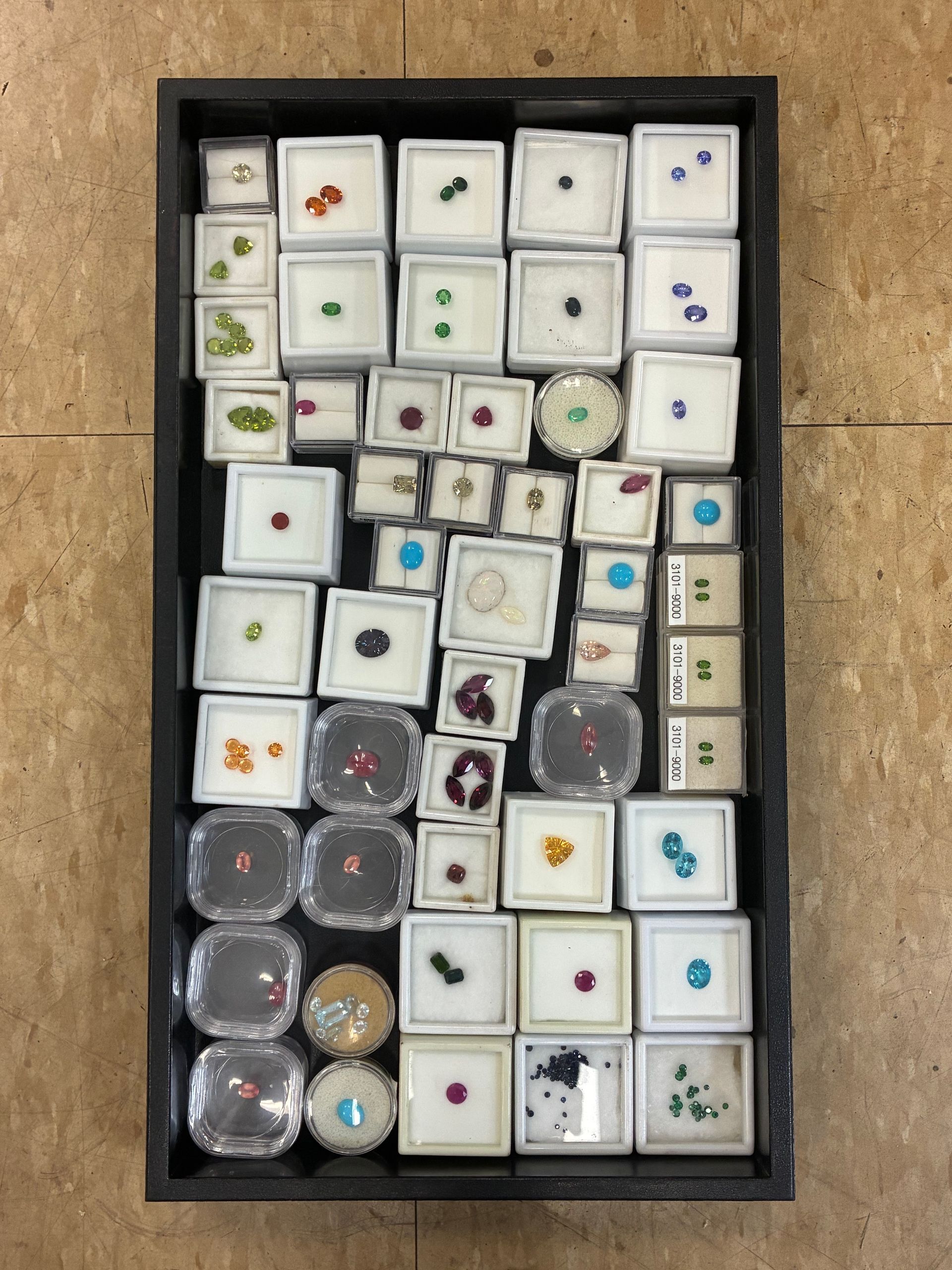 Tray of assorted small jewelry or trinket boxes arranged in a grid, mostly white with colorful designs.