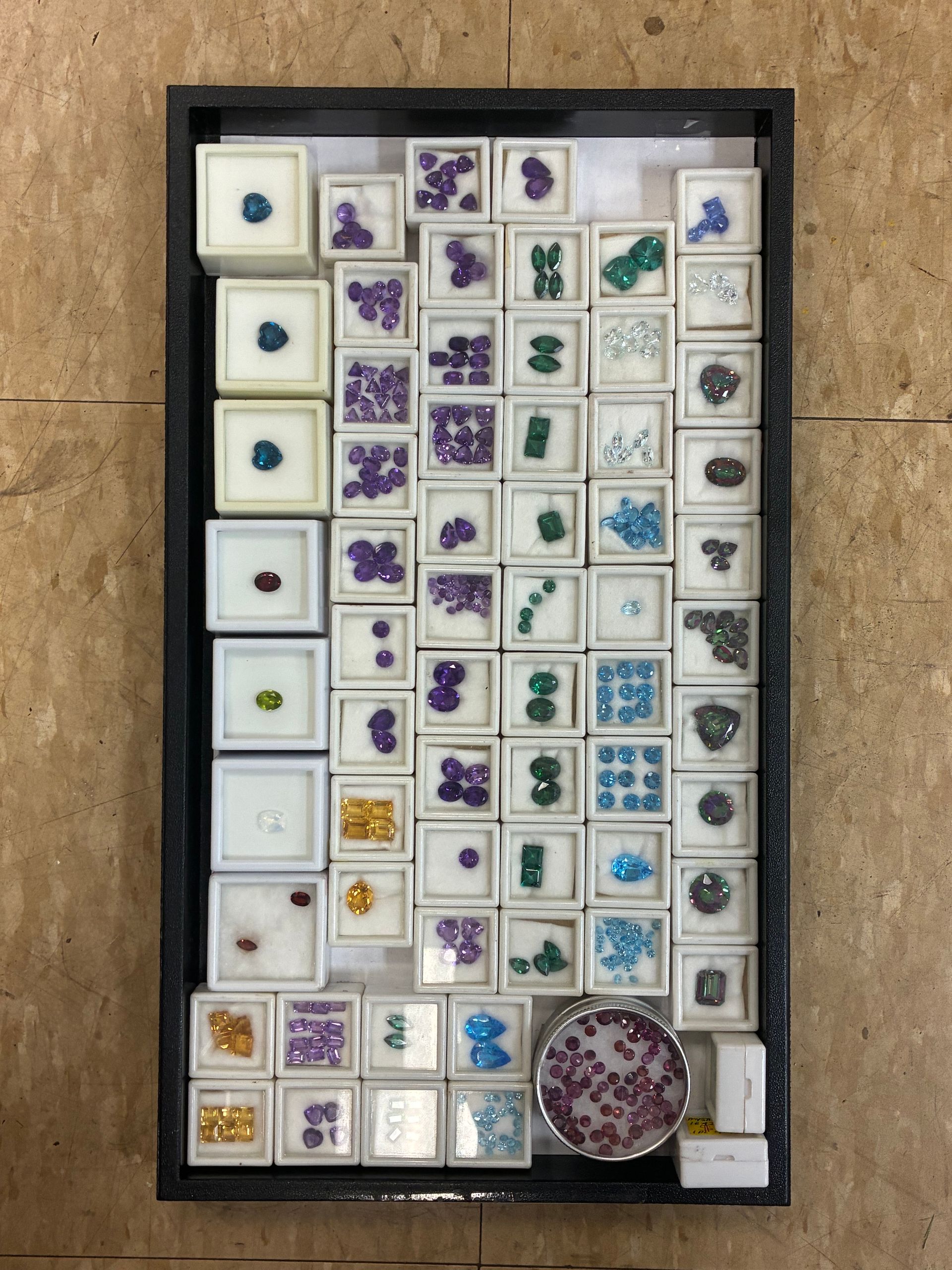 Tray of small square floral tiles and stones arranged in rows on a tan floor