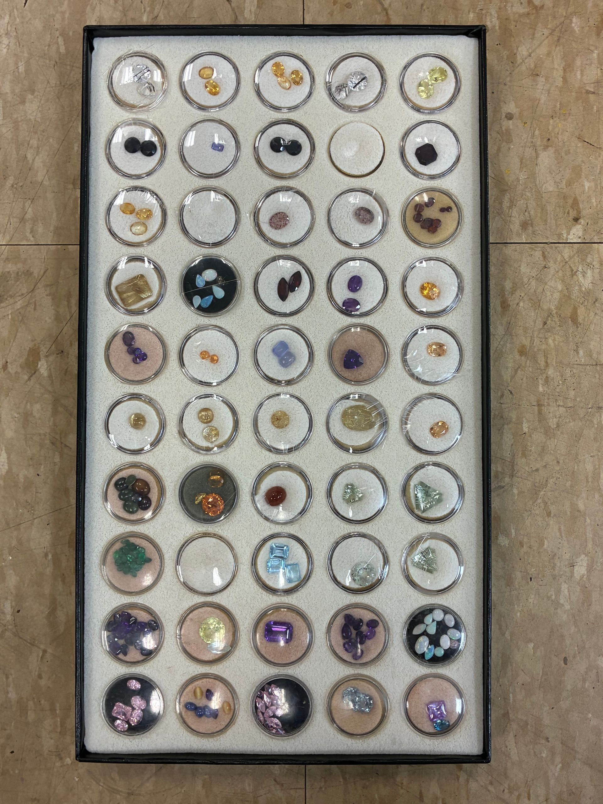 Tray of many small round jewelry pieces or buttons arranged in a grid on a beige surface.