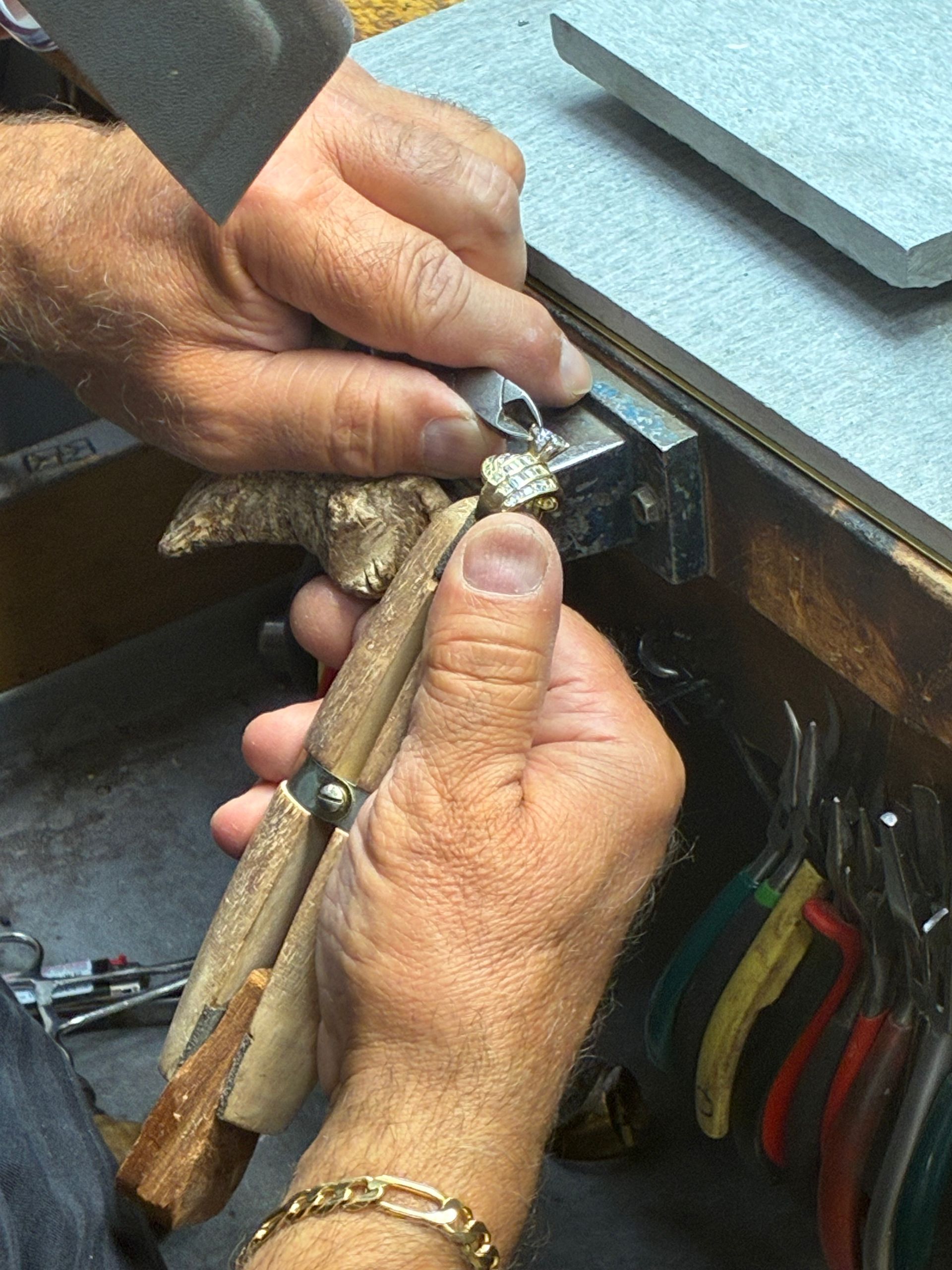 Hands using pliers to repair a small black device on a workbench.