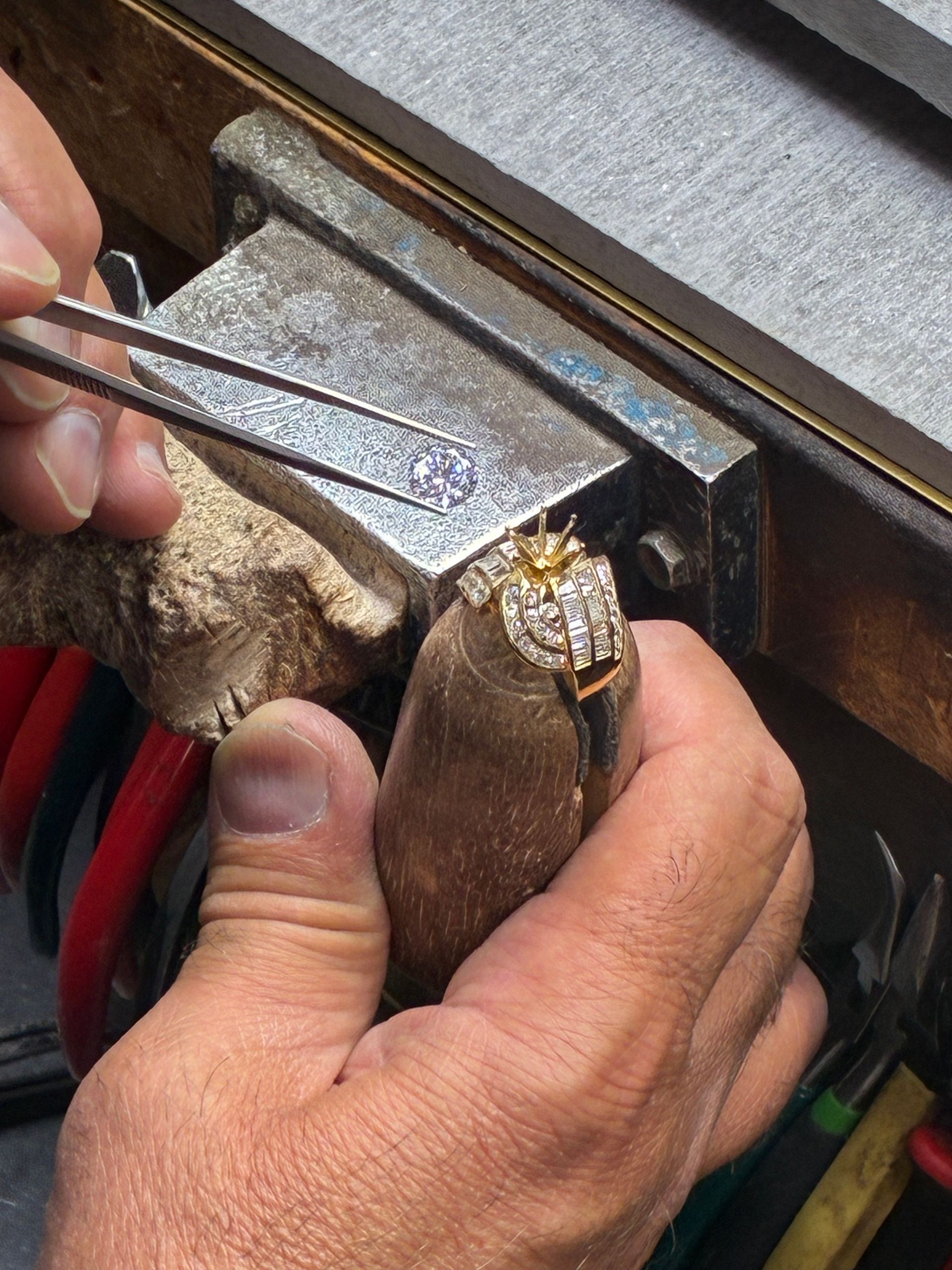 Hands filing a small metal piece clamped in a bench vise.