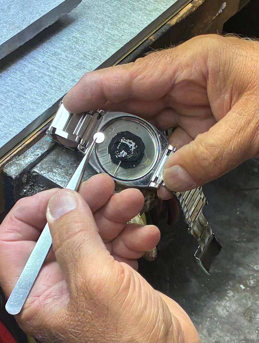 Hands using a caliper to measure a small round metal part on a workbench.