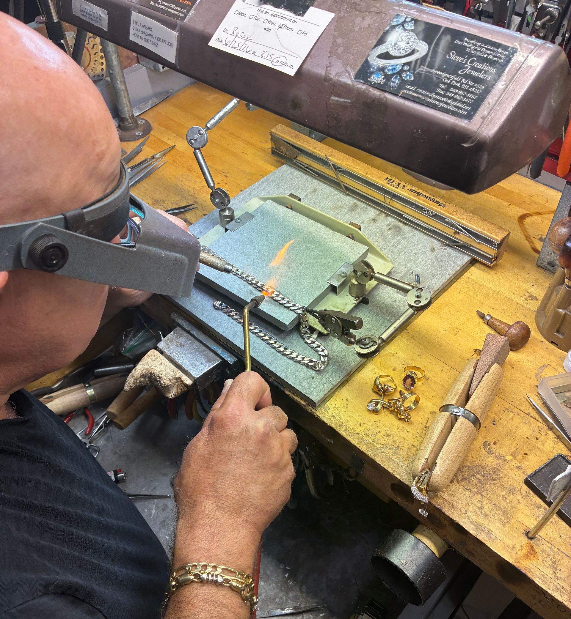 Person soldering a circuit board at a cluttered workbench with tools and wires