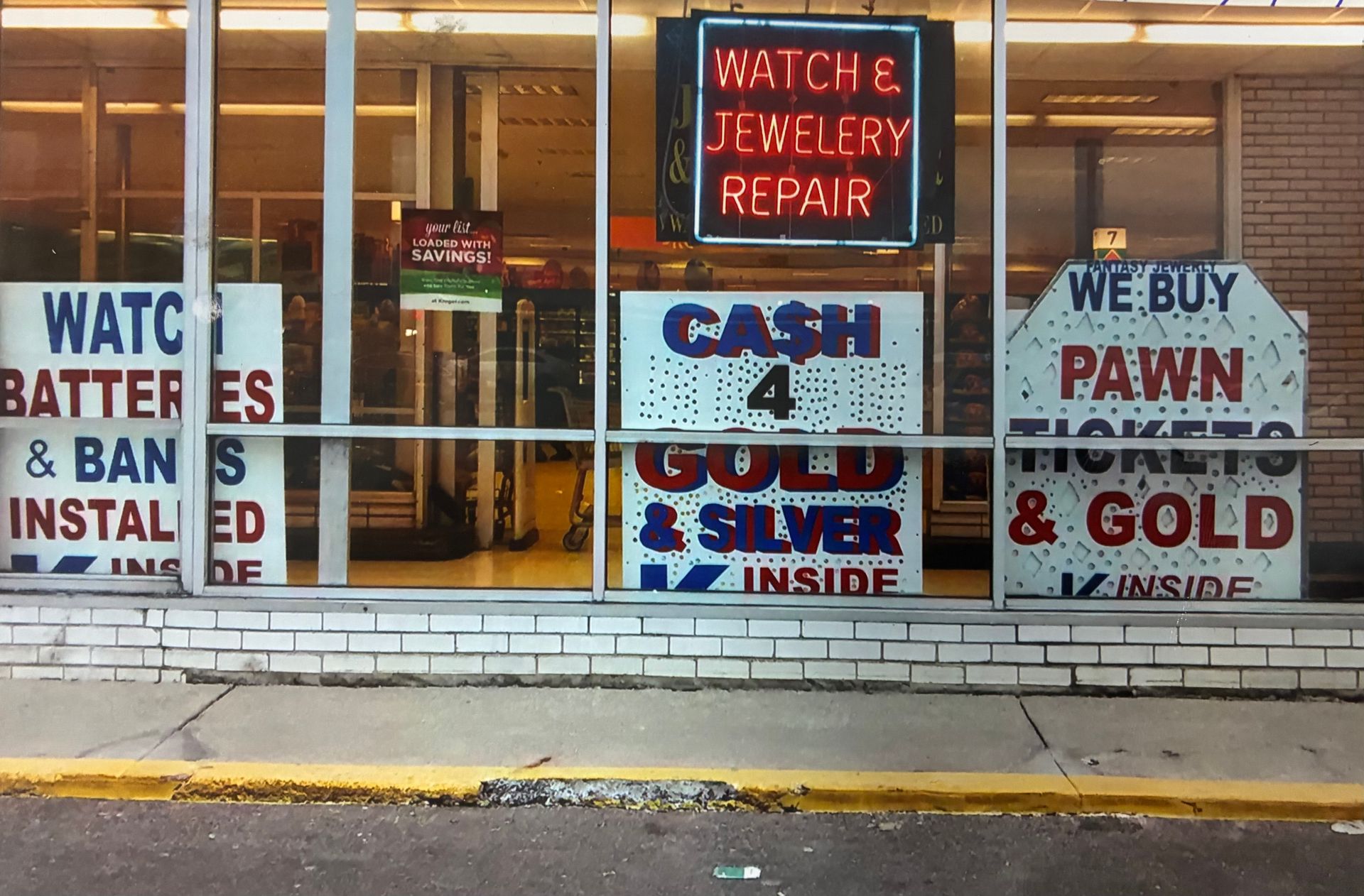 Pawn shop storefront with signs for watch repair, cash for gold, and buying watches, batteries, and bands.