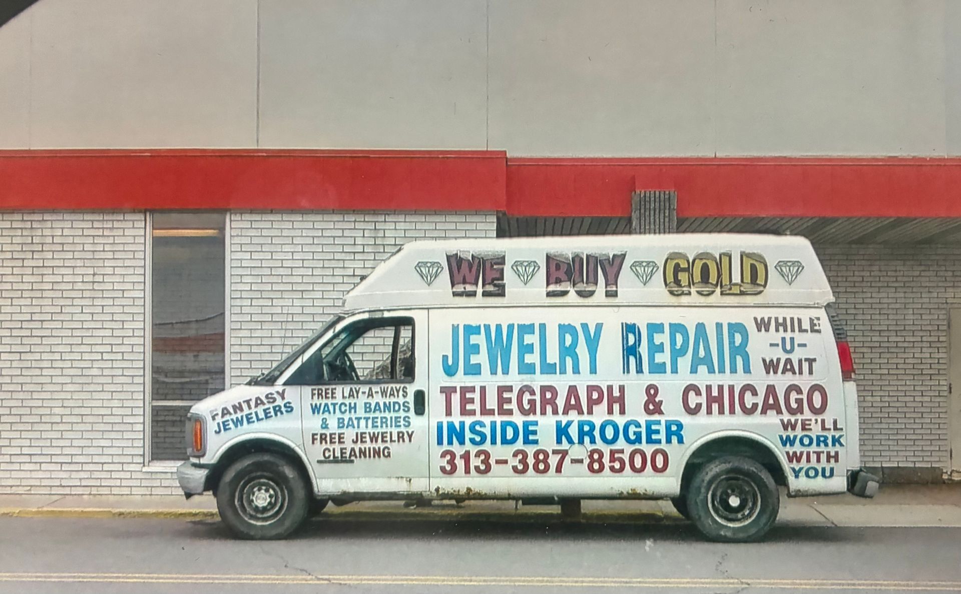 White vintage van with colorful “Jewelry Repair” and “Telegraph & Chicago” lettering parked by a brick wall.