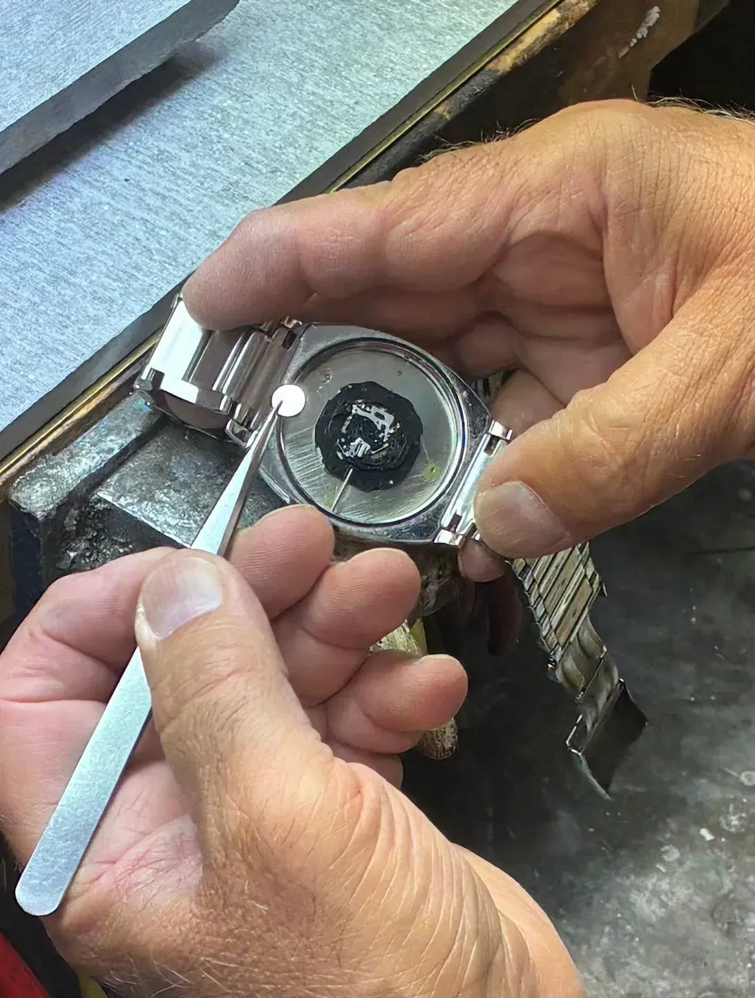 Hands holding a small metal lock mechanism and tool on a workbench.