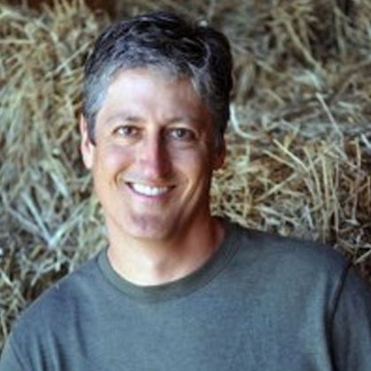 A man is smiling in front of a pile of hay