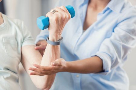 Una donna aiuta una donna anziana a sollevare un manubrio blu.