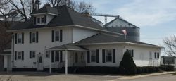 White two-story house with dark roof, porch, and black shutters on a corner lot