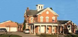 Red-brick building with white columns and a tower under a blue sky, with a parked van nearby