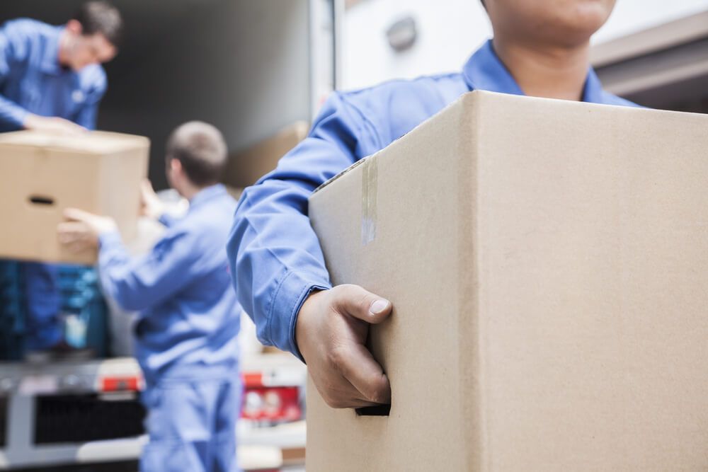 A Man Is Carrying a Cardboard Box in Front of A Truck — A-Team Delivery Services Pty Ltd in Cessnock, NSW