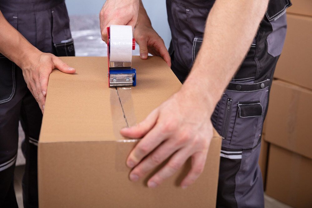 Two Men Are Taping a Cardboard Box With Tape — A-Team Delivery Services Pty Ltd in Maitland, NSW