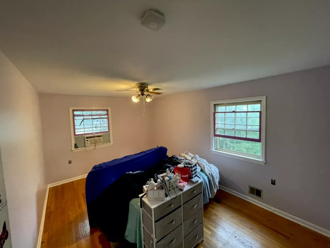 A bedroom with a couch , dresser , and two windows.