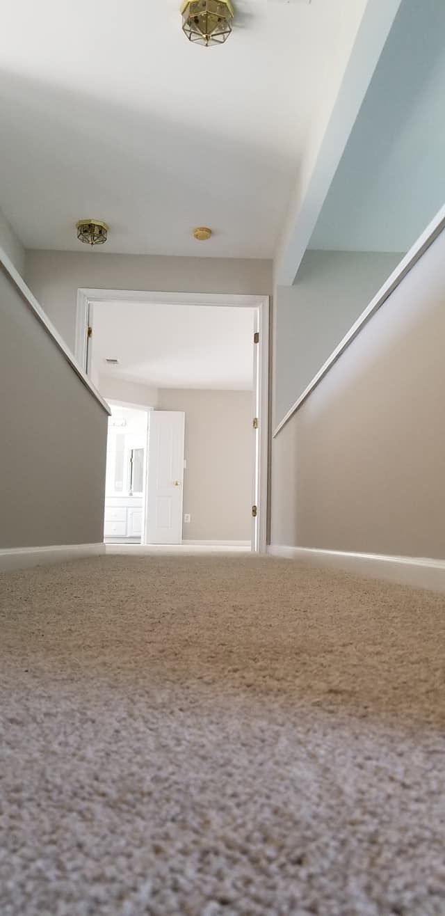 A hallway with a carpeted floor and a door leading to a room.