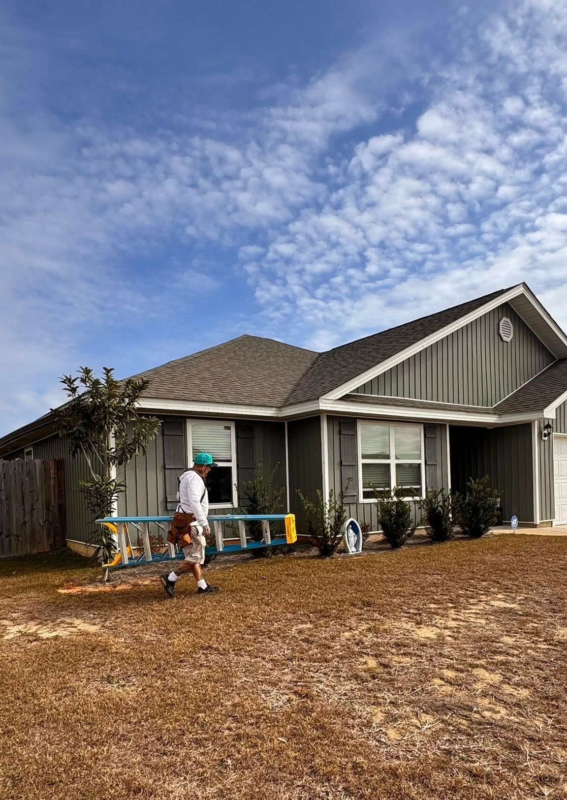 A single-story white house with a modern slanted roof sits behind a gravel driveway and lawn under a clear blue sky.