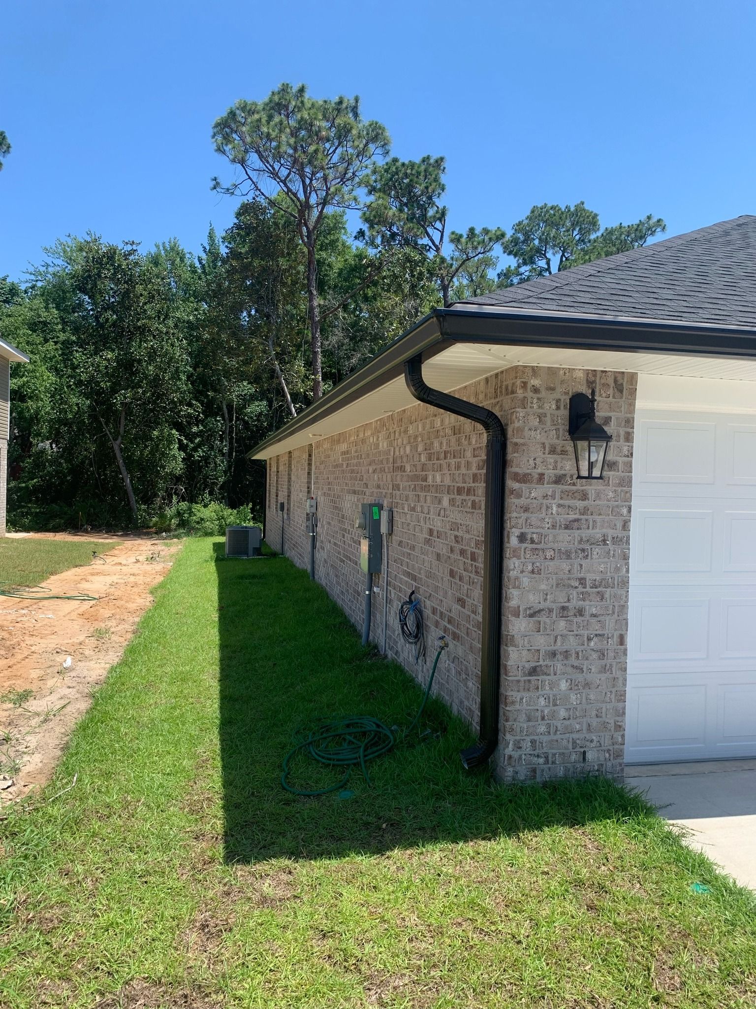 Side view of a light brick house with a white garage door, green lawn, and trees under a blue sky