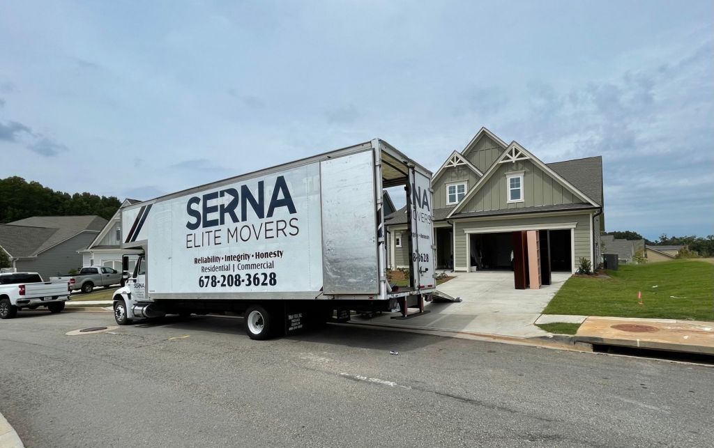 Moving truck parked beside a gray house on a driveway under a cloudy sky