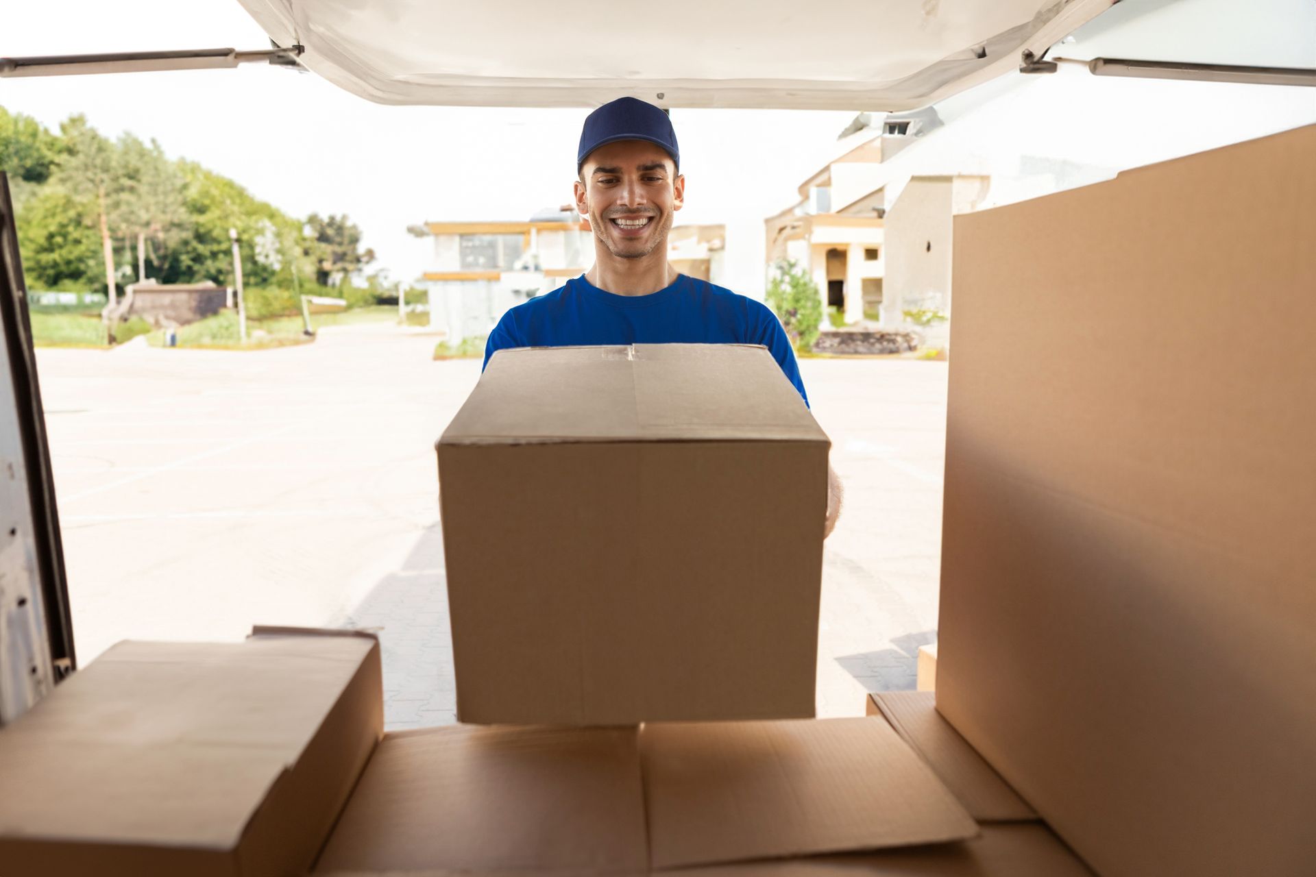 Delivery person holding a box, smiling at the camera, standing in the back of a van.