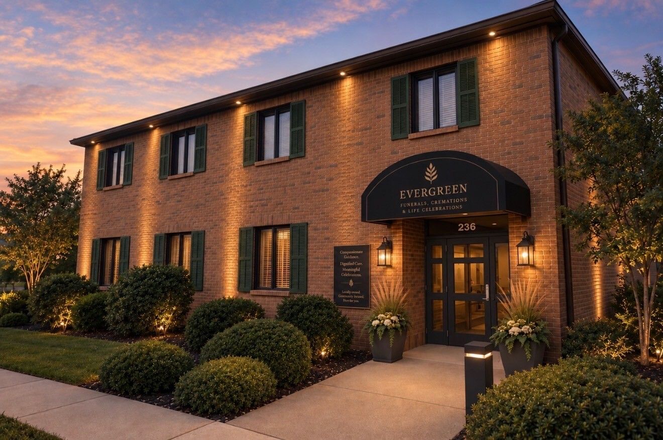 Brick hotel entrance at dusk with lit doorway, manicured shrubs, and a sunset sky