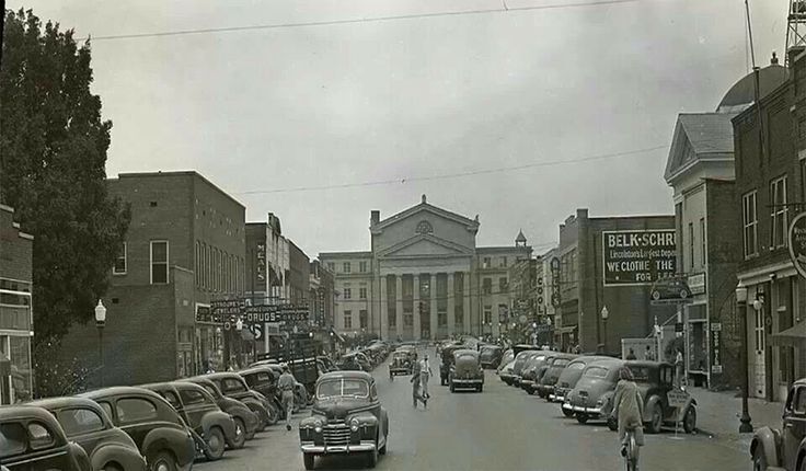 Cloudy street view with parked cars leading to a neoclassical building at the end of the road