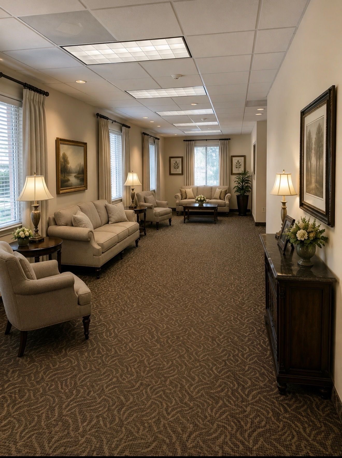 Elegant hallway lounge with beige sofas, chairs, lamps, and framed art along a carpeted corridor.