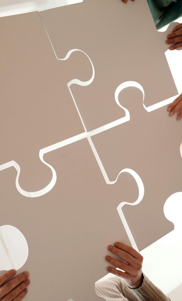 Verschillende mensen houden vier grote, blanco witte puzzelstukken omhoog terwijl ze beginnen ze in elkaar te passen.
